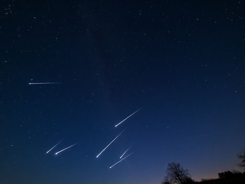 A wide-angle night sky photograph showing multiple Lyrids meteors streaking across a star-filled sky, with the constellation