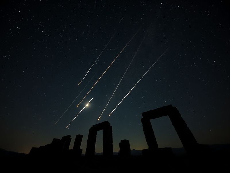 A wide-angle night sky photograph featuring the Lyrid meteor shower, with meteors streaking above a serene landscape with sil