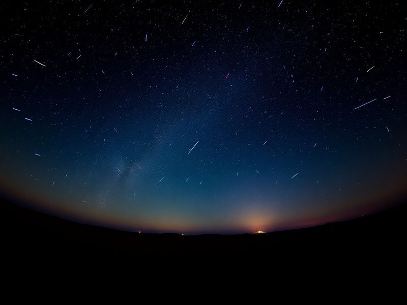 A wide-angle night sky photograph featuring multiple Lyrids meteors streaking across a star-filled sky, with the Milky Way vi