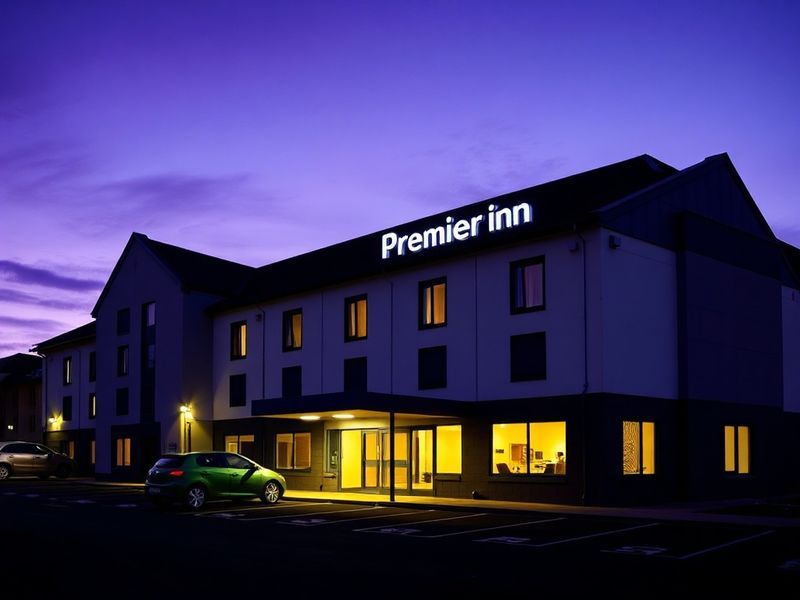 A modern Premier Inn hotel exterior at dusk, featuring the brand’s signature blue and white signage, with a few guests enteri