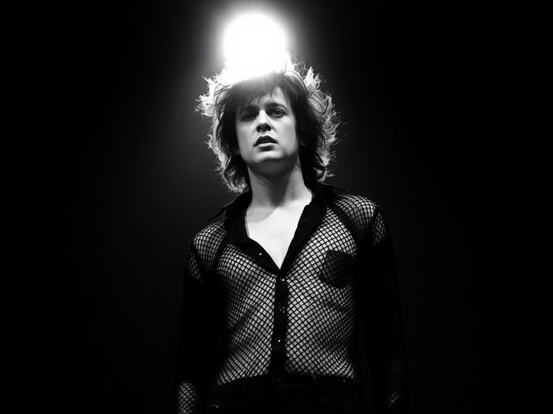A moody, atmospheric portrait of Robert Smith in a dimly lit room, wearing his signature smudged lipstick and dark eyeliner,