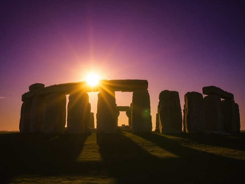 A vibrant scene of people celebrating the summer solstice at Stonehenge during sunrise, with the ancient stones silhouetted a